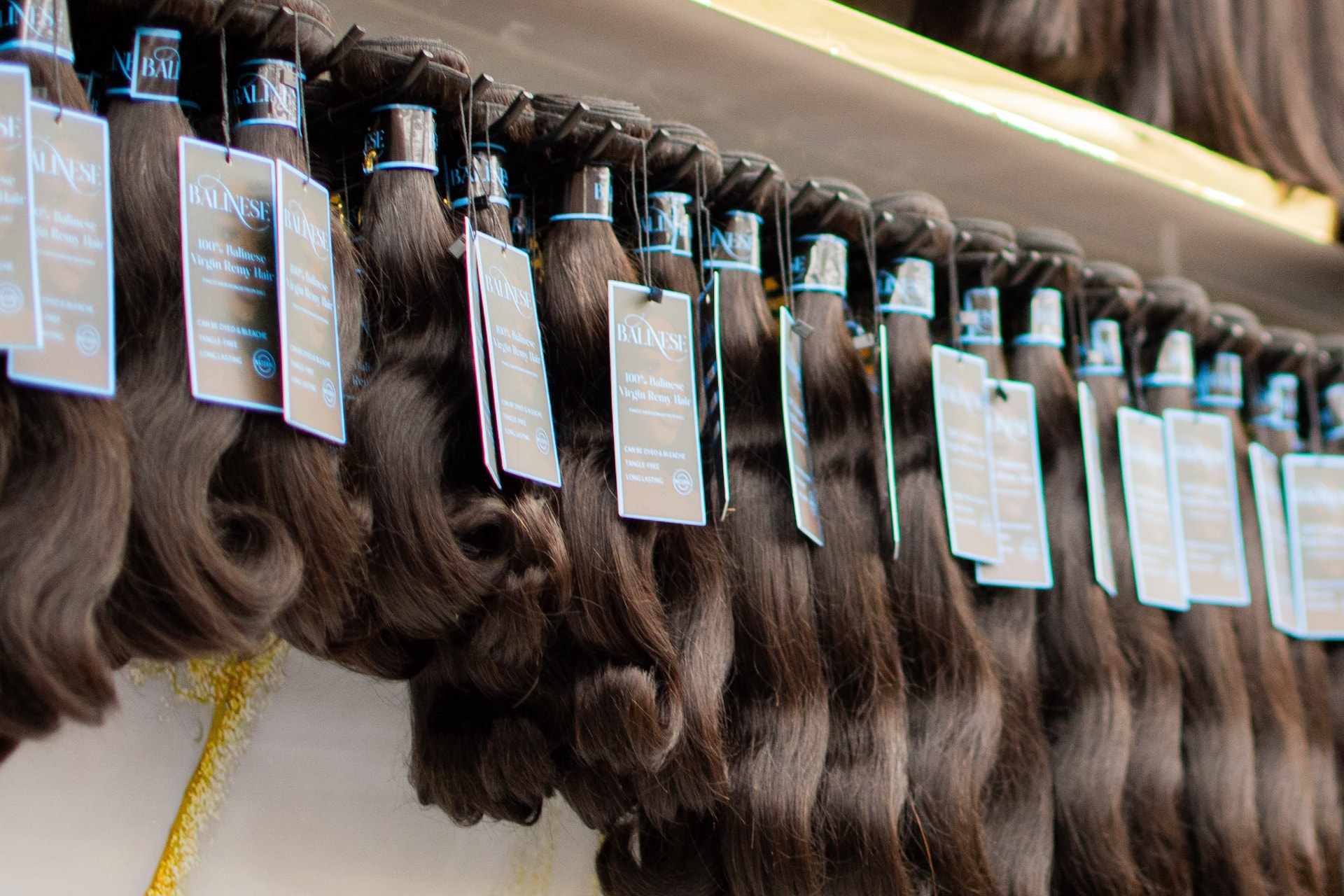 Rows of Balinese virgin remy human hair bundles hanging on display with brand tags